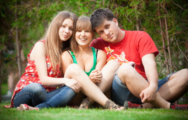 Two girls and young man sitting on meadow with crossed legs