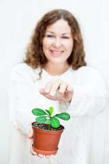 Young positive woman covering green plant by hands