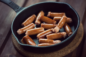 Cast-iron pan with fried mini sausages, horizontal shot