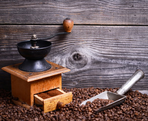 Manual coffee grinder with beans and vintage scoop on wooden bac