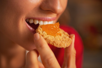 Portrait of young woman eating cookie with orange jam