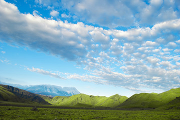 landscape of green meadow, mountain, blue sky and clouds, Russia