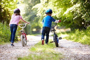 Two Children Pushing Bikes Along Country Track