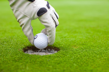 Man's hand putting a golf ball into a hole on the green field