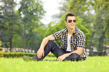 Handsome guy with sunglasses sitting on grass