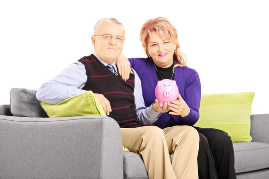 Mature couple sitting on a sofa and holding a piggy bank