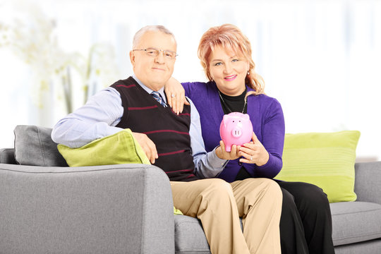 Mature man and woman on sofa holding a piggy bank at home