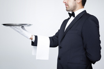 Professional waiter holding an empty silver tray over gray backg