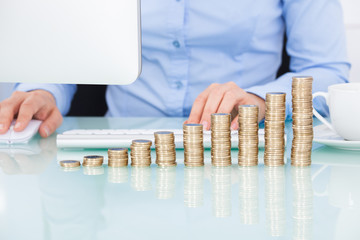 Coins Stacked On Desk In Front Of Businesswoman