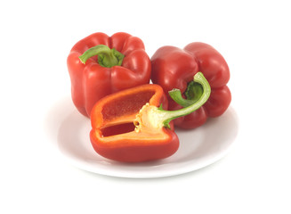Three whole red ripe bell peppers on a plate isolated