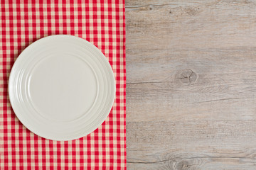 Empty plate on tablecloth on wooden table. Top view.