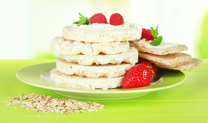 Tasty crispbread with berries on plate, on green table