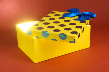 Gift box with bright light on it on red background