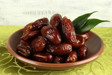 Dried dates on plate on tablecloth on wooden background