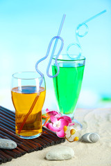 Glasses of cocktails on sand, on bright background