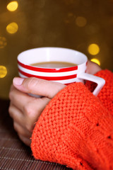 Hands holding mug of hot drink, close-up, on bright background