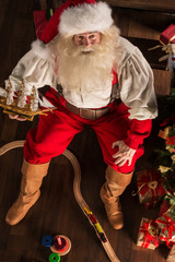 Santa Claus at home playing with new toys near Christmas Tree
