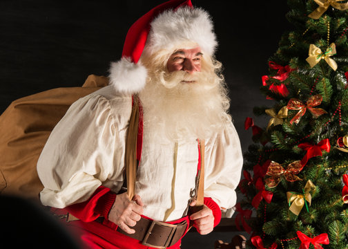 Real Santa Claus carrying big bag full of gifts, at home near Ch