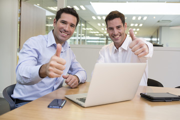Successful Businessmen in office, looking camera, with thumbs up