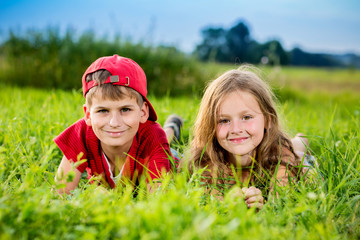 Cut boy and a girl are resting on the green grass in summer