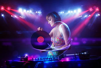 Disc jockey girl playing music with light beam effects on stage