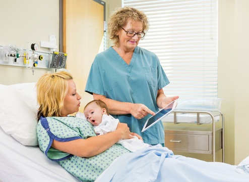 Nurse Explaining Reports On Digital Tablet To Woman With Babygir