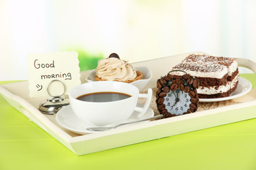 Cup of tea with cakes on wooden tray on table in room