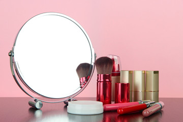 Round table mirror with cosmetics on table on pink background