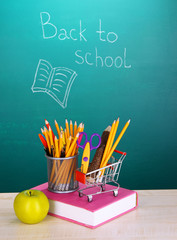 School supplies in supermarket cart on blackboard background