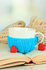 Cup with knitted thing on it and open book close up