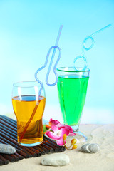 Glasses of cocktails on sand, on bright background