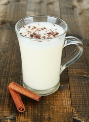 Cup of eggnog with cinnamon on wooden background