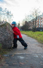 Little boy pushes a large rock