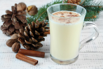 Cup of eggnog with fir branches on wooden background