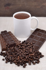 White cup of hot chocolate on coffee beans and chocolate backgro