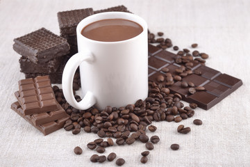 White cup of hot chocolate on coffee beans and chocolate backgro
