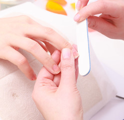 Beautician with file filing nails female client. Beauty salon