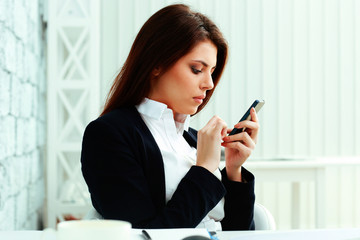 Young serious businesswoman typing on her smartphone in office