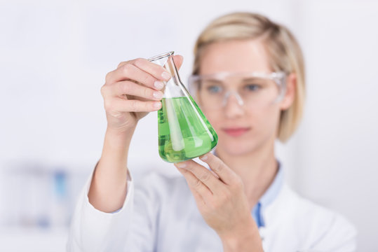 chemielaborantin schaut auf glaskolben mit flüssigkeit