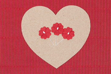 Cardboard heart with paper flowers on red background.