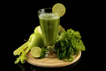 Glass of green vegetable juice and vegetables isolated on black