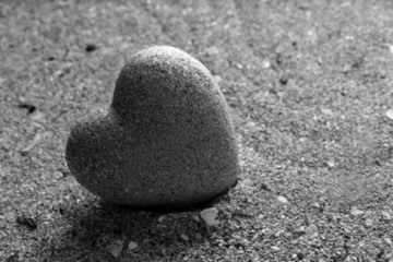 Fototapeta na wymiar Szary kamień w kształcie serca, na tle piasku