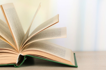Opened book on wooden table on bright background