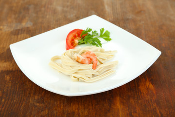 Pasta with shrimps on white plate, on wooden background