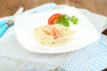 Pasta with shrimps on white plate, on wooden background