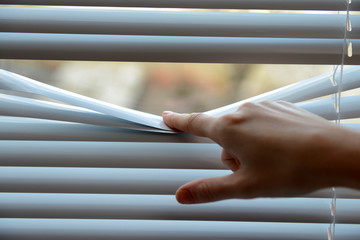 Female hand separating slats of venetian blinds with a finger