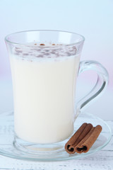 Cup of eggnog with cinnamon on table on bright background