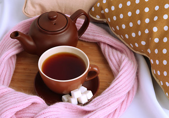 Cup and teapot with scarf on bed close up