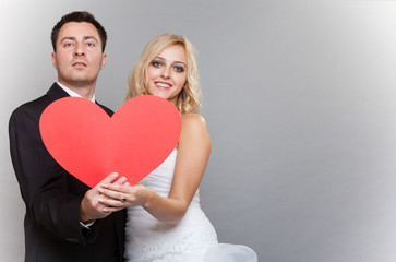 Fototapeta na wymiar Portrait of happy bride and groom with red heart on gray