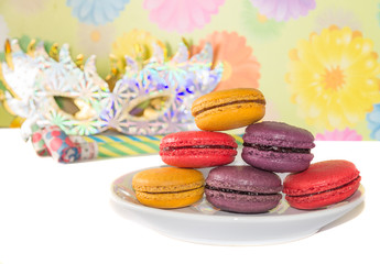 Sweet colorful macaron against festive masks and pipes